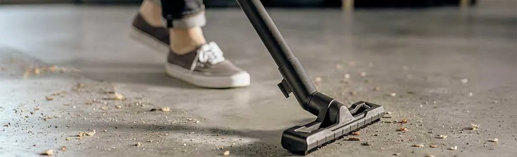 Someone is vacuuming the floor with a Kärcher vacuum cleaner, picking up visible dirt and debris.