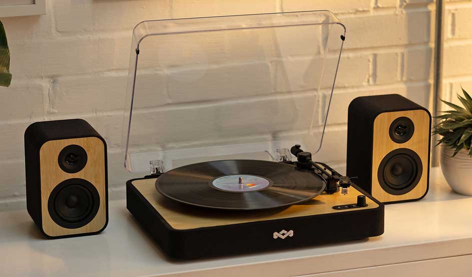 A House of Marley record player with wooden details and two matching speakers stands on a cabinet, with a vinyl on the turntable.