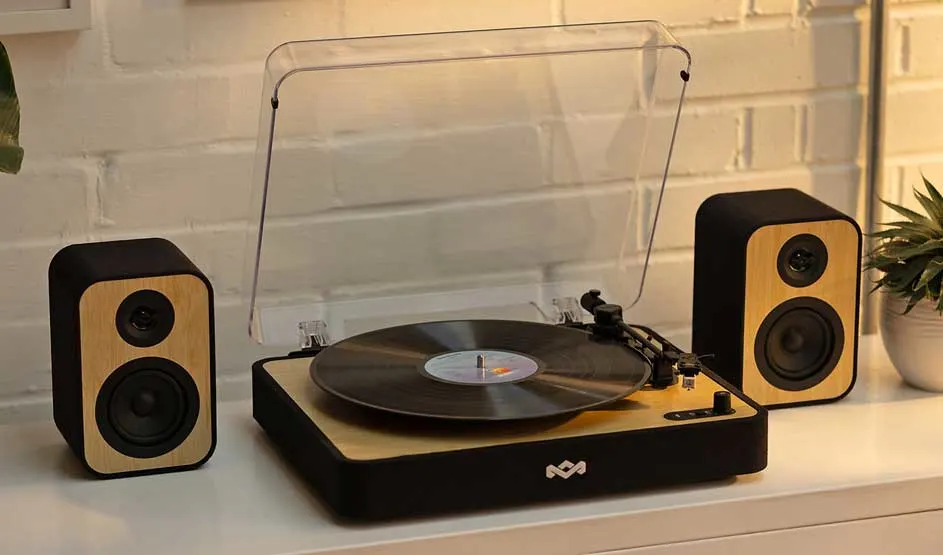 A House of Marley record player with wooden details and two matching speakers stands on a cabinet, with a vinyl on the turntable.