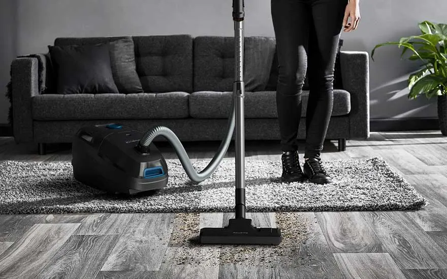 Een traditionele sledestofzuiger verwijdert vuil van zowel tapijt als houten vloer, efficiënt en krachtig in de woonkamer.