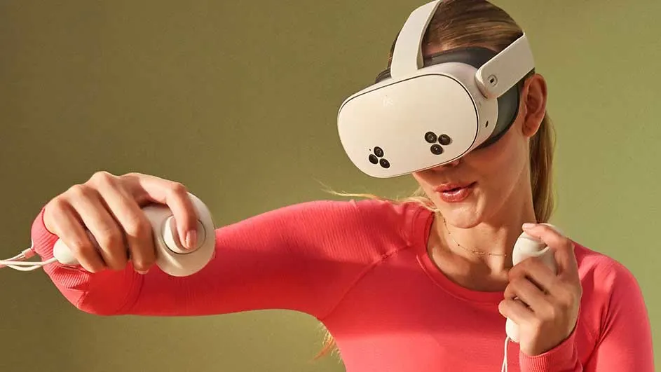 Een vrouw met een VR-bril en controllers staat voor een groene achtergrond. Ze draagt een roze shirt.