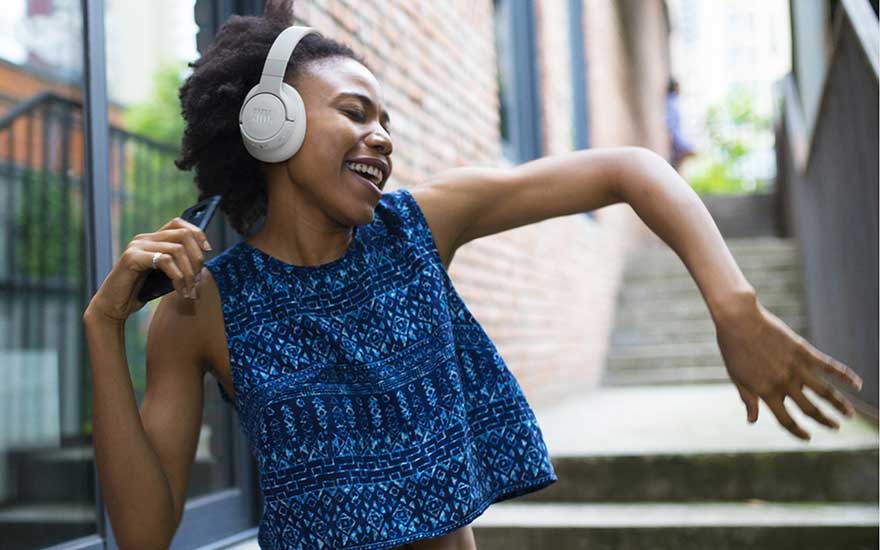 Woman with white headphones dances joyfully in an alley outdoors, phone in hand, completely absorbed in the music.