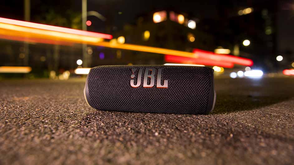 Een zwarte JBL-luidspreker ligt op straat 's nachts, met lichtstrepen en gebouwen op de achtergrond.