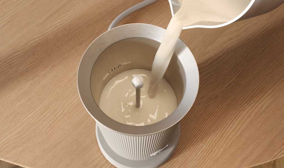 Melk wordt uit een witte kan in een open melkopschuimer gegoten, op een houten tafel, met de roerstaaf duidelijk in het midden.