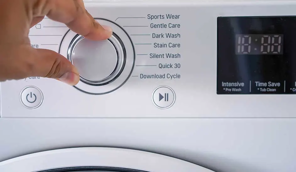 Een hand draait aan de programma-knop van een wasmachine. Op het display staan diverse wasprogramma’s en een digitaal scherm.