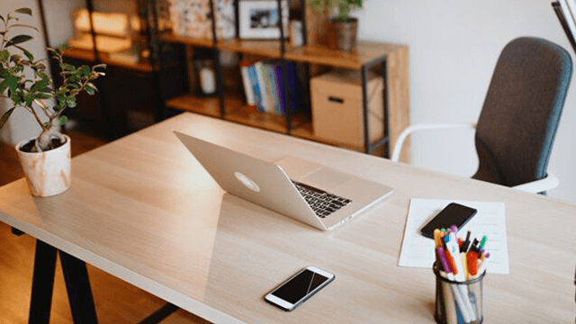 Bureau met laptop, plant, pennen, document en twee telefoons. Op de achtergrond een bureaukast en een bureaustoel.