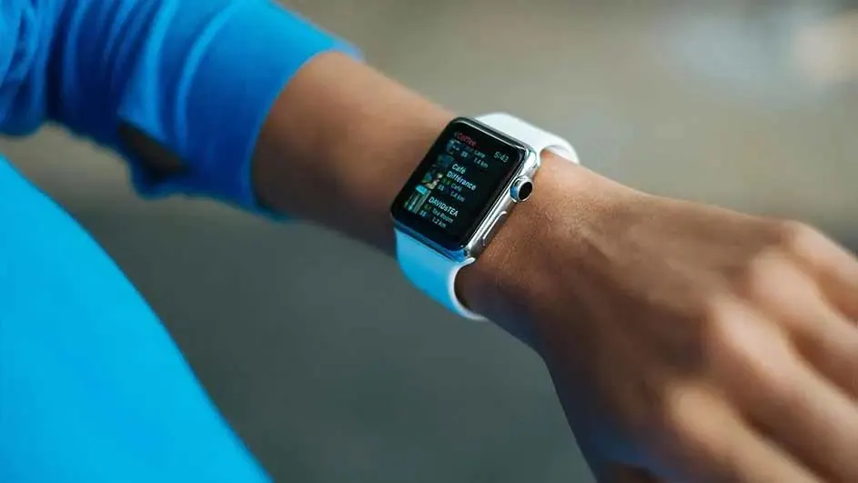 Close-up of a person in a blue top wearing a white smartwatch, its small screen showing colourful fitness stats on their wrist.