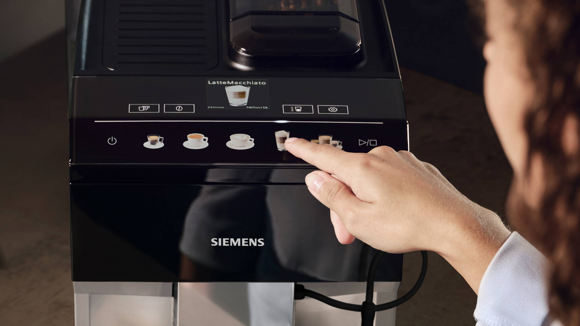 Een hand selecteert een drankje op een zwart Siemens koffiezetapparaat met diverse koffie-opties.