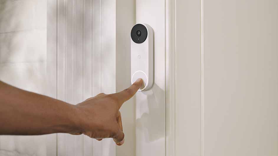A finger presses a white doorbell with a black camera on a white paneled door.