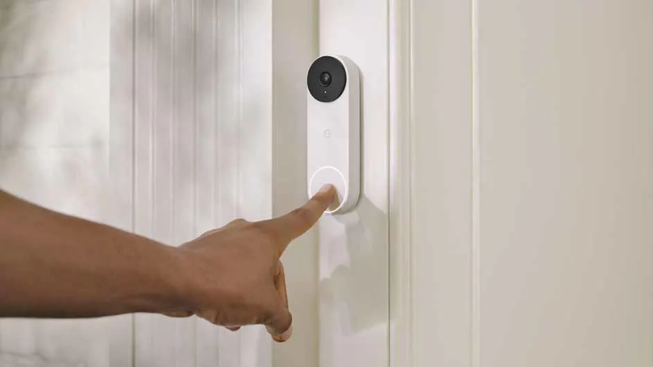 A finger presses a white doorbell with a black camera on a white paneled door.
