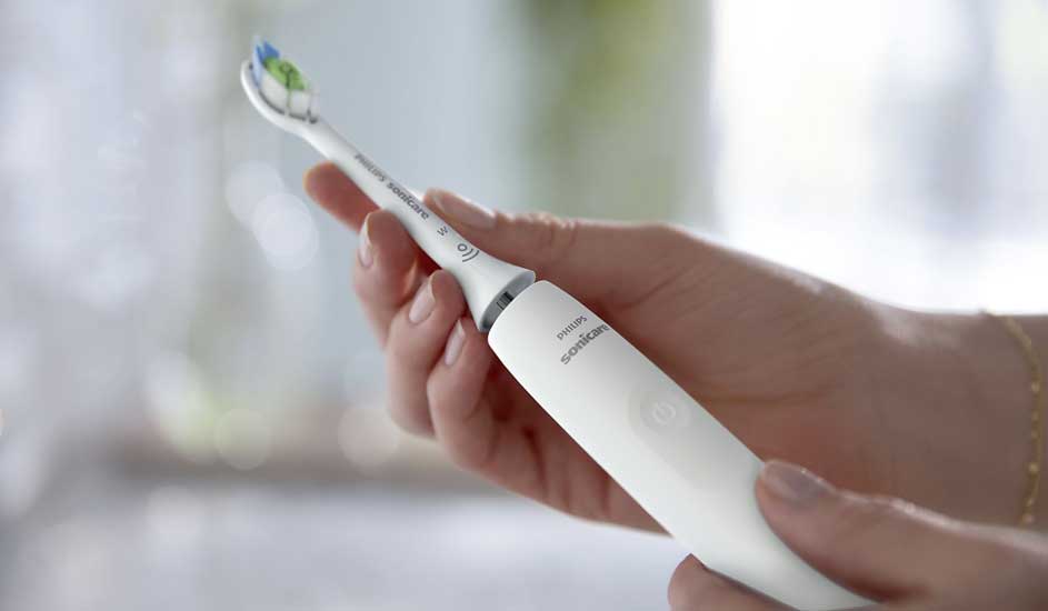 Een hand houdt een witte elektrische tandenborstel van het merk Philips vast, met zachte achtergrondverlichting en een frisse uitstraling.