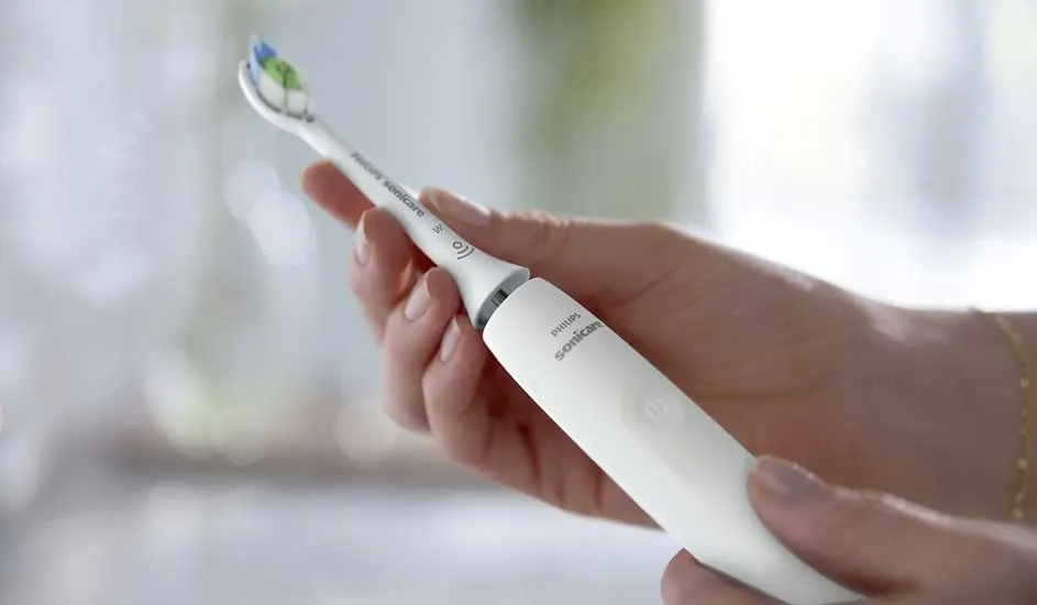 Een hand houdt een witte elektrische tandenborstel van het merk Philips vast, met zachte achtergrondverlichting en een frisse uitstraling.
