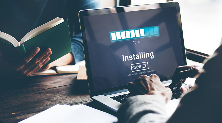 Een persoon gebruikt een laptop met een installatiebalk op het scherm, terwijl iemand anders een boek leest.