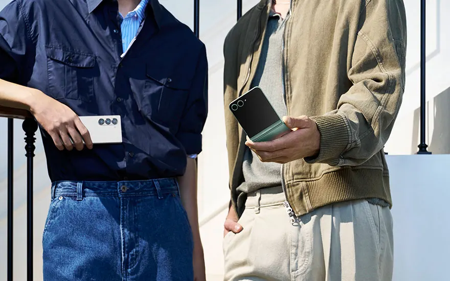 Twee personen in casual kleding houden Samsung smartphones vast, een met wit toestel en een met zwart toestel, staand bij moderne reling.