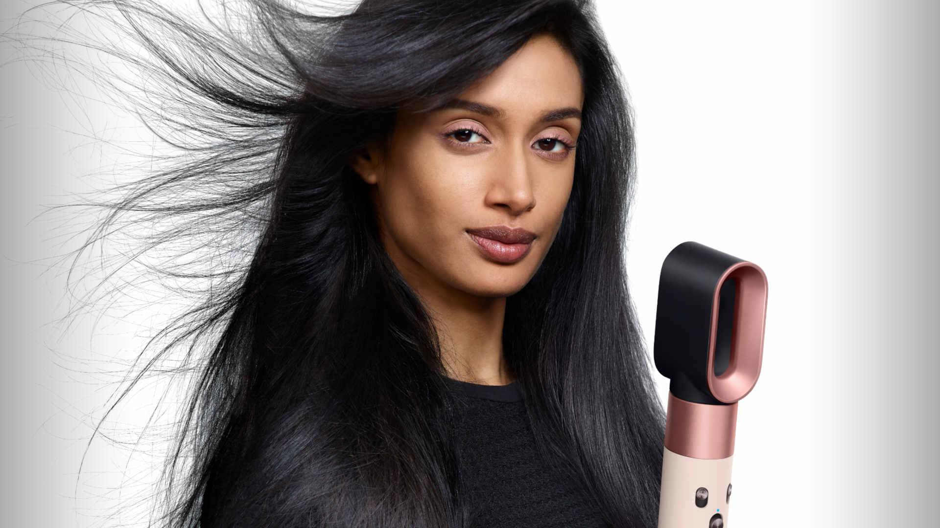 Lang, zwart haar wordt gestyled met een roségouden en zwarte föhn; enkele haren staan statisch uit.