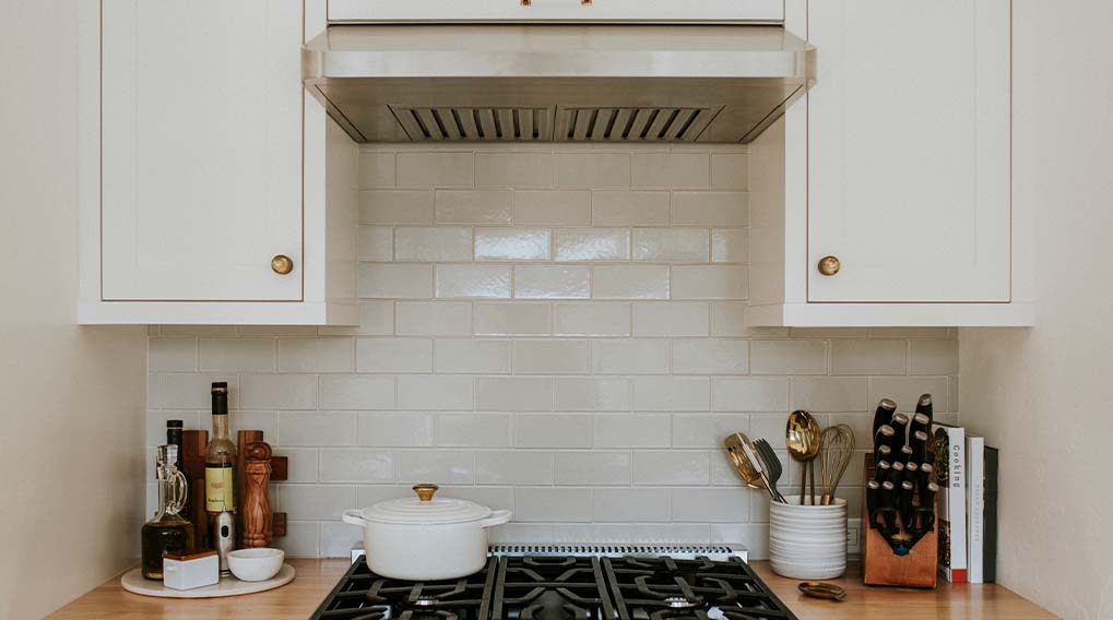 Keuken met witgoed, tegels en een fornuis. Er staan kookgerei en potten op het aanrechtblad.