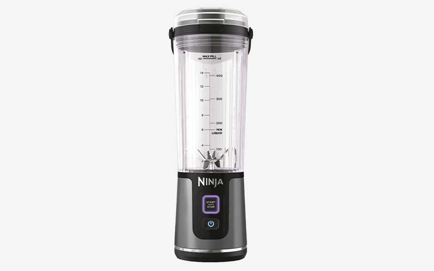 Een draagbare blender met transparante beker, maatverdeling en mesjes staat rechtop op een witte achtergrond.