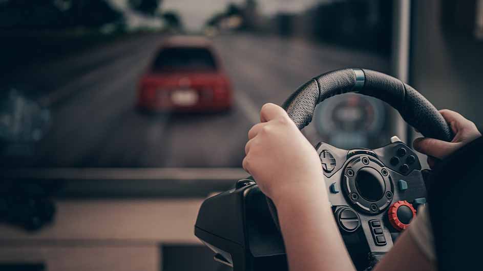 Handen houden een zwart stuur met knoppen vast; op de achtergrond een scherm met een grijze weg en een rode auto.