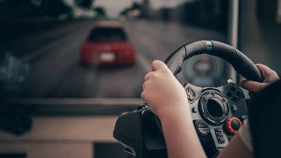 Handen houden een zwart stuur met knoppen vast; op de achtergrond een scherm met een grijze weg en een rode auto.