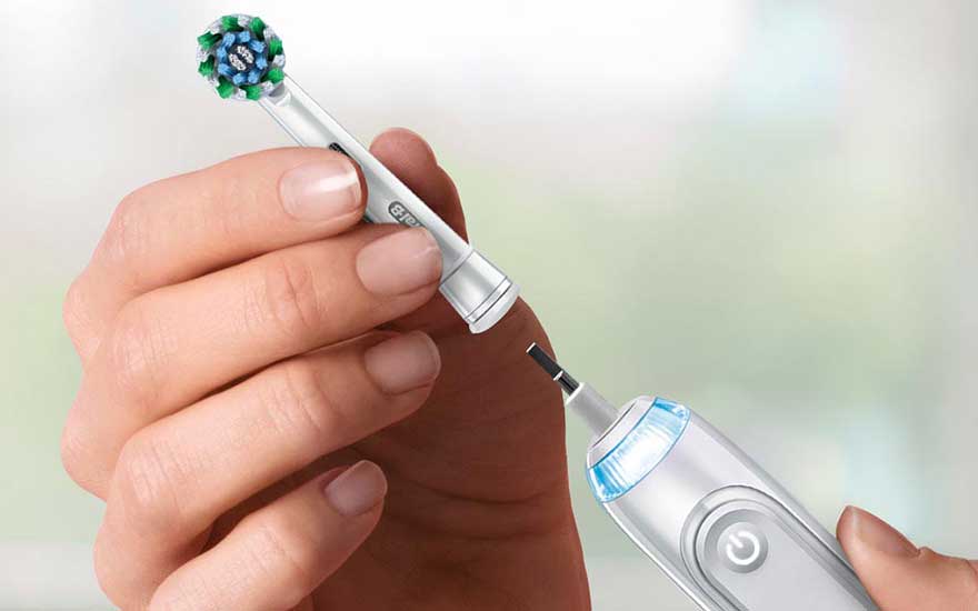 Hands remove the brush head from an electric toothbrush, focusing on the simple replacement of the detachable attachment.