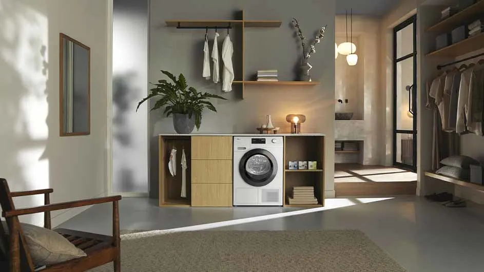 Waskamer met wasmachine, houten kast, plant, decoratie en kleding aan rekken. De kamer is modern en minimalistisch ingericht.