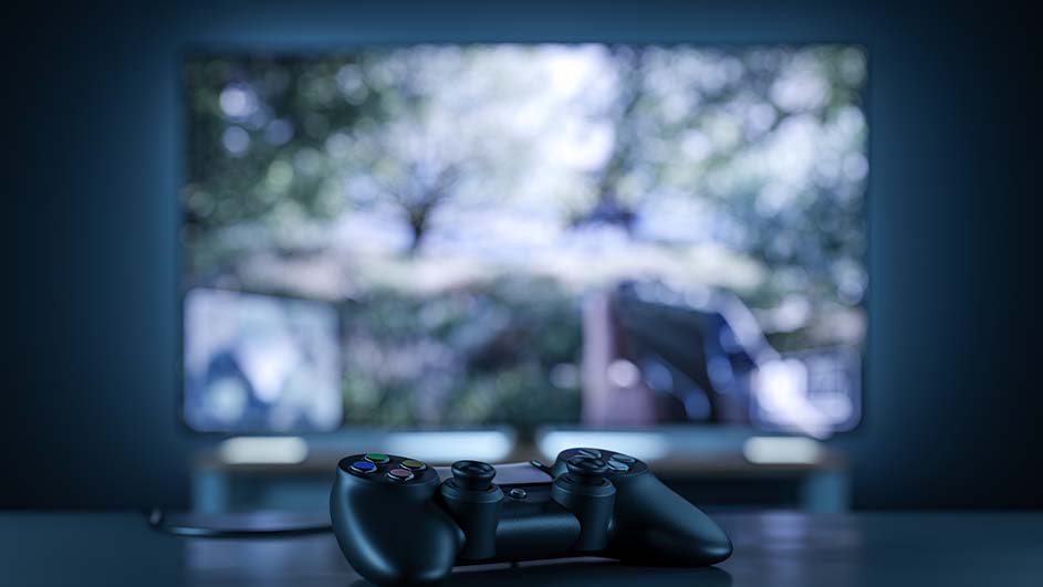 Een zwarte gamecontroller ligt voor een televisie met een wazig beeld van bomen en een figuur.