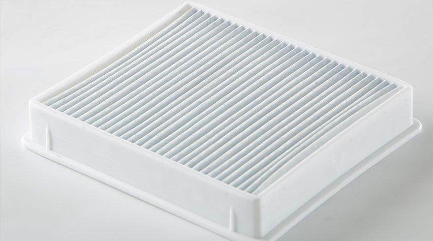 Een wit vierkant filter met parallelle plooien in een witte frame op een witte achtergrond.