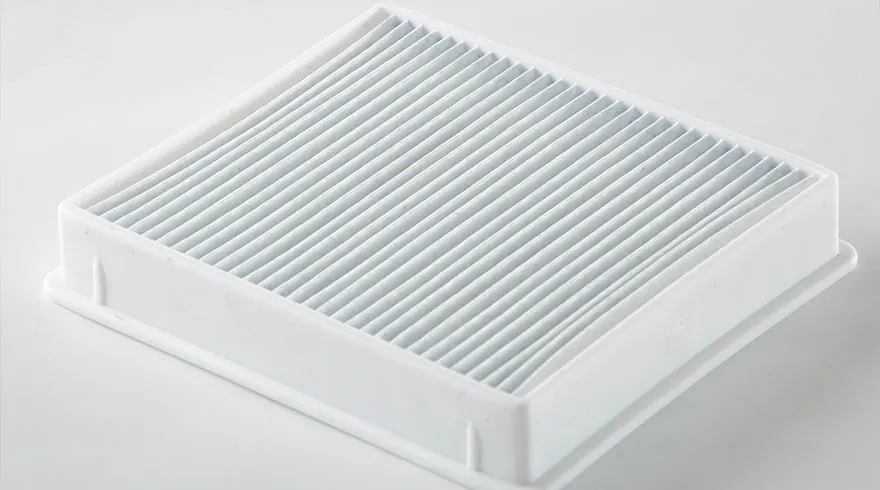 Een wit vierkant filter met parallelle plooien in een witte frame op een witte achtergrond.