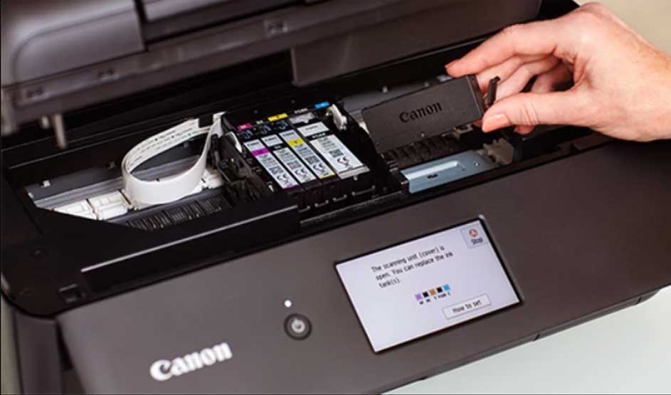 Een hand vervangt een Canon inktcartridge in een zwarte Canon printer met touchscreen. Het Canon-logo is duidelijk zichtbaar.