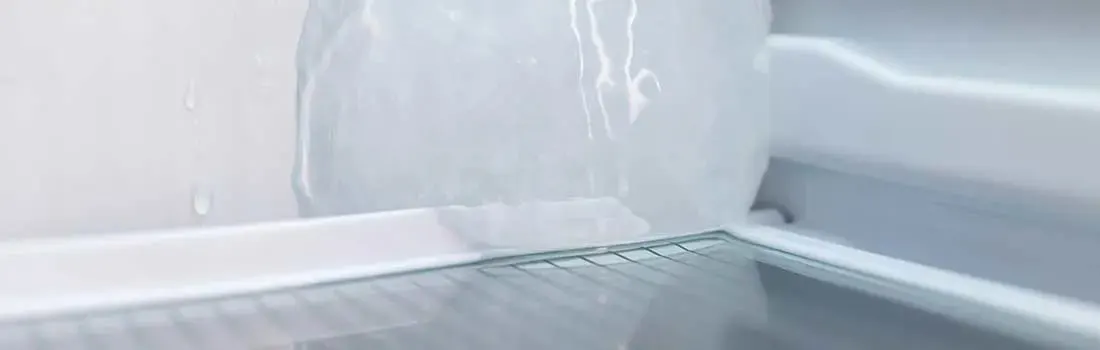 Dikke ijsbult groeit tegen de achterwand van een vriesvak, met glanzend bevroren oppervlak en druppels die erboven langs lopen.