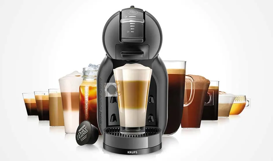 Op de afbeelding staat een zwarte KRUPS NESCAFÉ Dolce Gusto koffiemachine, omringd door verschillende glazen koffievariaties.