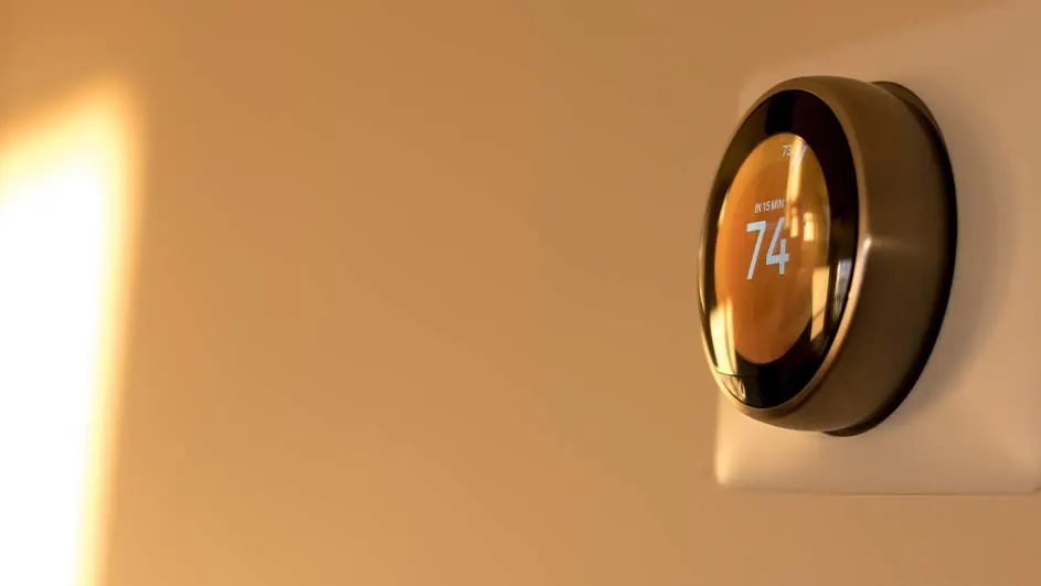Ronde thermostaat aan de muur, met een display waarop '74' staat. Zachte lichtinval links.