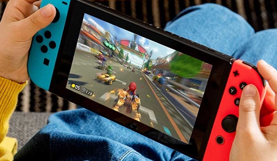 Iemand speelt Mario Kart op een Nintendo Switch met blauwe en rode controllers, zittend met blauwe broek en gele trui.