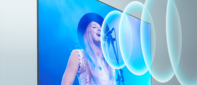 Een vrouw met een hoed zingt in een microfoon, weergegeven op een televisiescherm met blauwe lichteffecten.