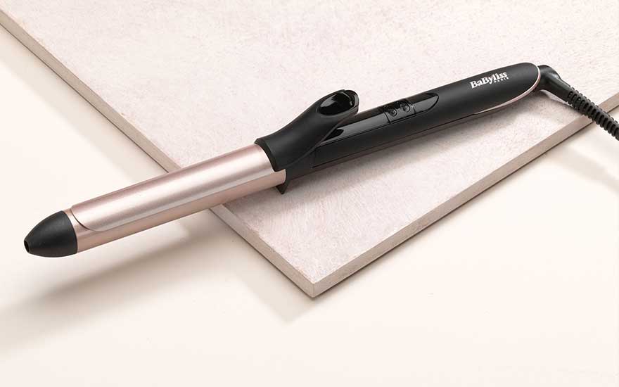 BaByliss curling iron with black handle and rose gold barrel resting on a white surface.