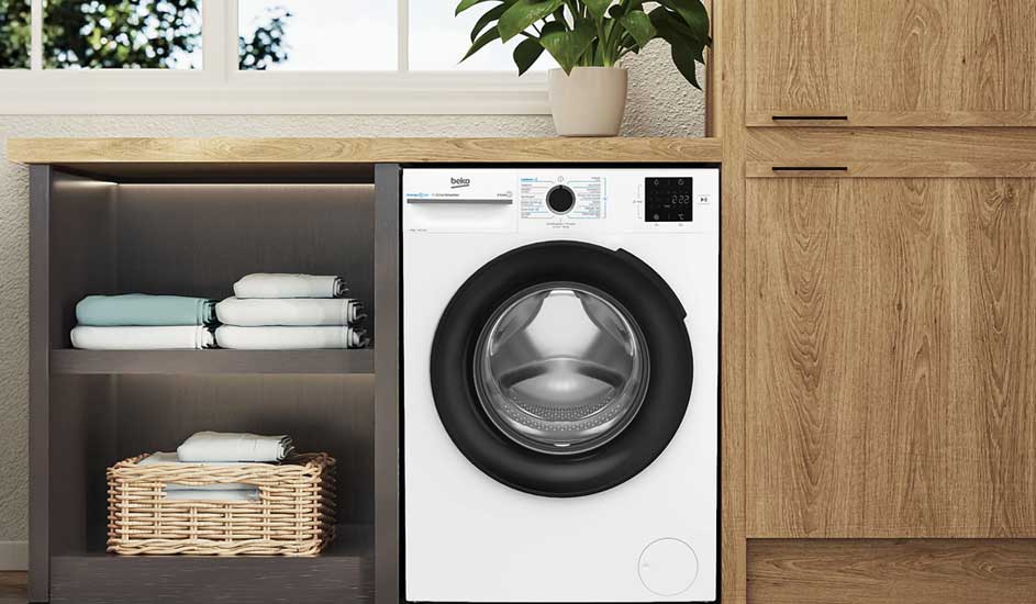 Een witte wasmachine met groot rond venster en digitaal display. Het bedieningspaneel toont programma's en opties. De machine staat in een lichte ruimte met zichtbare houten elementen.