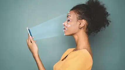 Een vrouw scant haar gezicht met een smartphone tegen een blauwe achtergrond. Blauwe lijnen accentueren de gezichtsscan.