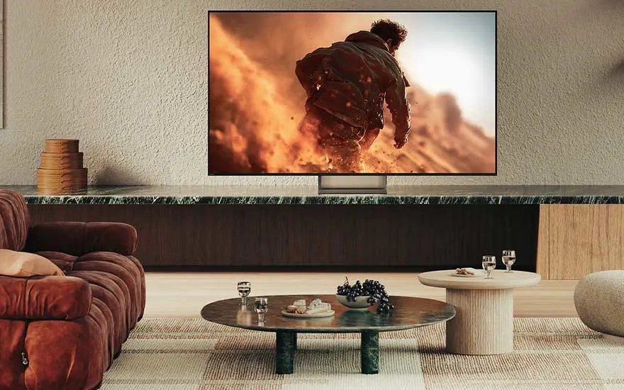 Moderne woonkamer met grote tv aan de muur, waarop een actiescène met rennende persoon in stofwolken speelt.