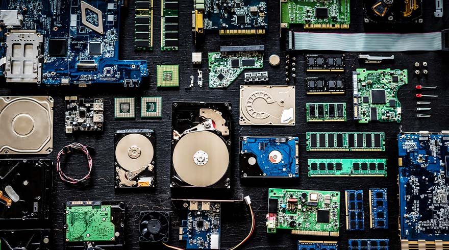 Diverse computeronderdelen, zoals harde schijven en moederborden, liggen verspreid op een donkere ondergrond.