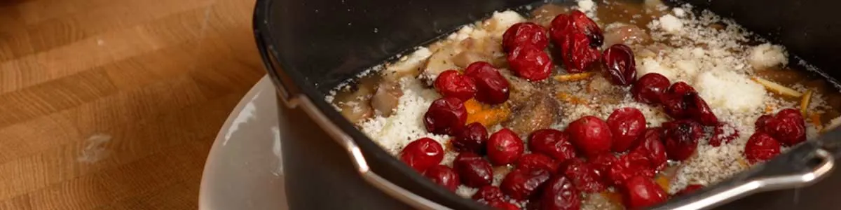 Ovenschaal met vlees, saus, geraspte kaas en verse rode bessen op een houten aanrecht.