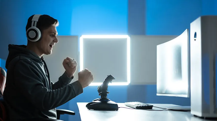 Een man met een koptelefoon zit achter een computer met een joystick, en balt zijn vuisten.