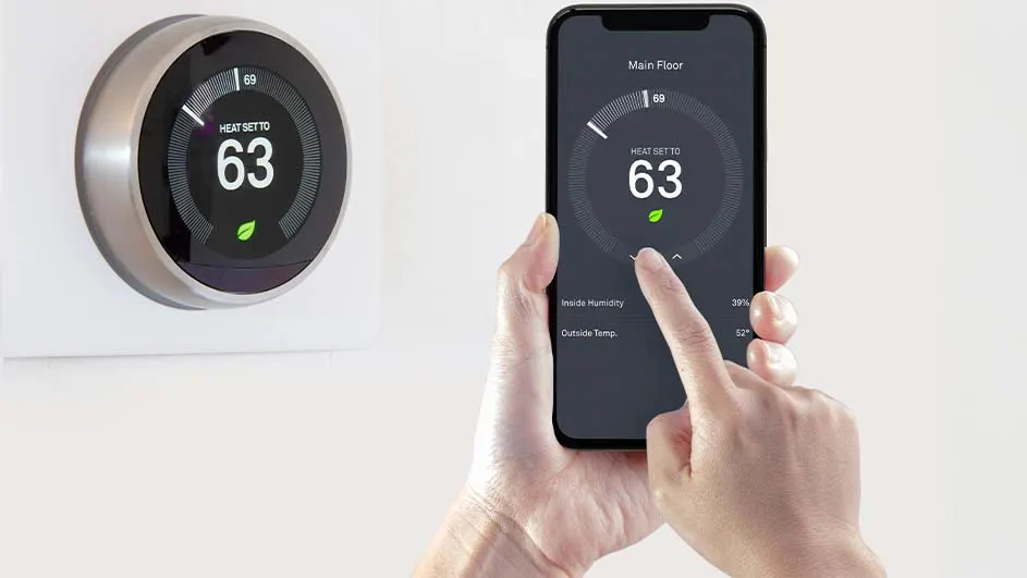 Een slimme thermostaat aan de muur en een telefoon in een hand tonen dezelfde temperatuur van 63 graden.