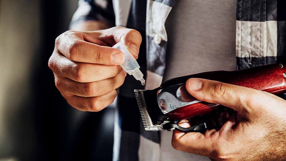 Een man smeert olie op een tondeuse met een klein flesje. De man draagt een geruit overhemd.