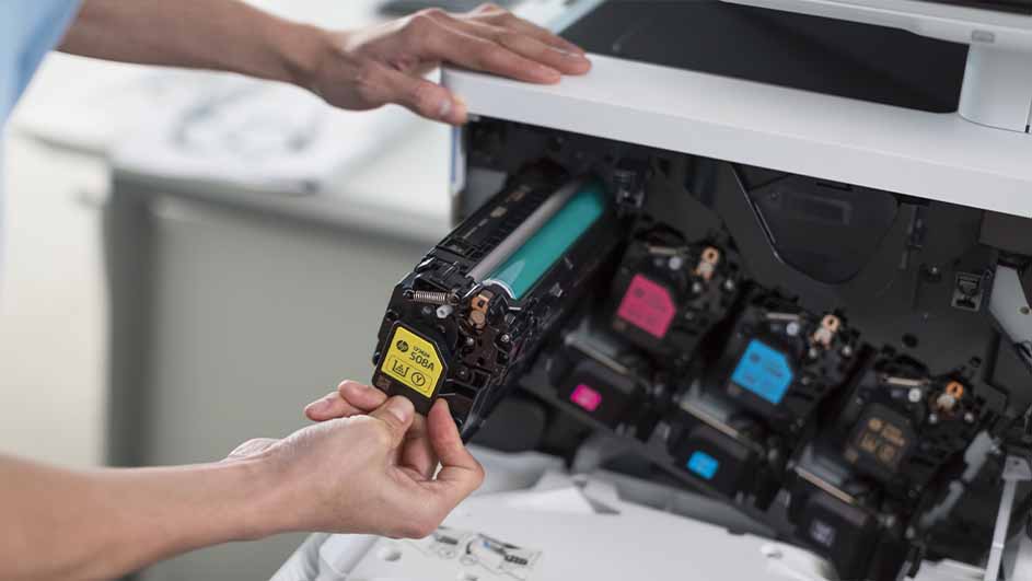 Een persoon vervangt een gele toner cartridge in een witte printer. Roze en blauwe cartridges zijn ook zichtbaar.