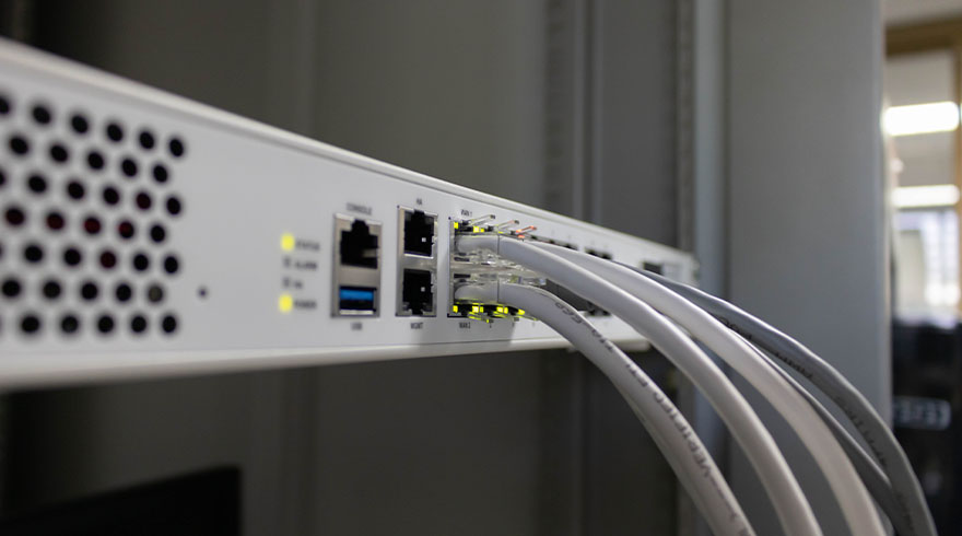 Een witte server met poorten en aangesloten grijze kabels tegen een grijze achtergrond, met indicatielampjes aan.