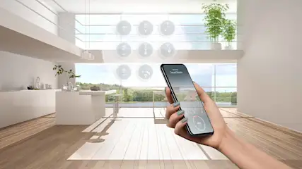 Hand houdt een telefoon met 'Smart Home' in een lichte kamer met houten vloer en grote ramen.