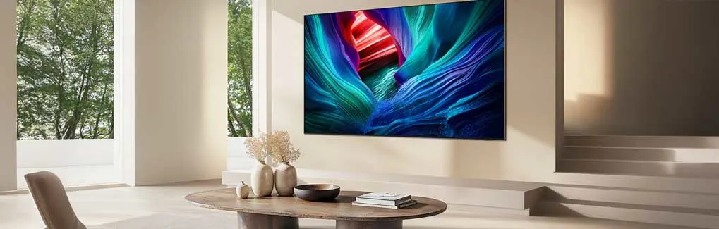 Een moderne woonkamer met grote tv aan de muur toont levendige blauwe en rode grafische inhoud. Minimalistisch design met houten tafel, bloemenvazen en natuurlijk licht van ramen.