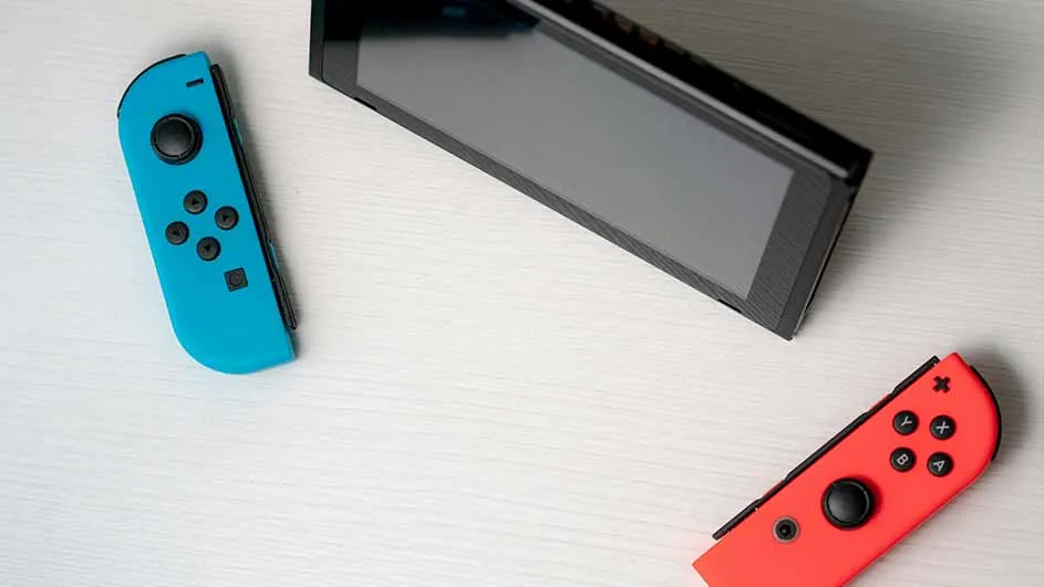 Een blauwe en rode Joy-Con-controller en een zwarte Nintendo Switch-console liggen op een witte ondergrond.