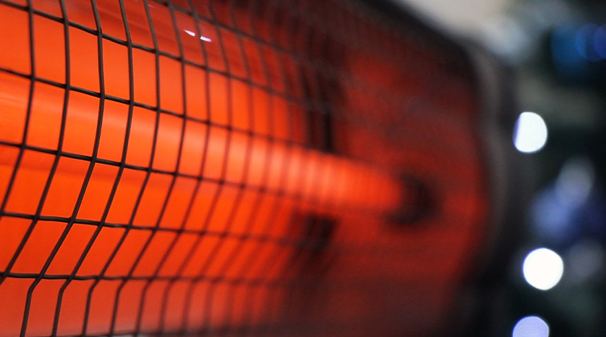 Een close-up van een oranje verwarmingselement achter een zwart metalen raster. Bokeh lichten in blauw en wit op de achtergrond.