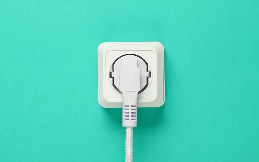 Een witte stekker zit in een wandstopcontact tegen een turquoise achtergrond, een eenvoudige illustratie van stroomvoorziening.